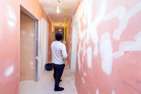 Worker is painting the ceiling by paint roller in corridor an apartment is inder Stock Photos