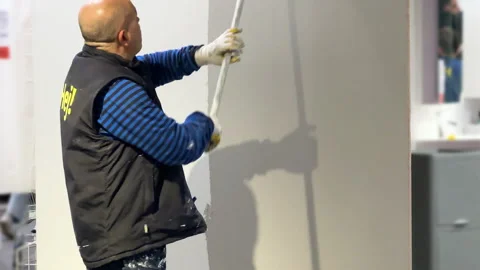Worker painting white wall in grey with roller in bright modern space Stock Footage 308019272