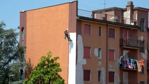 Worker paints a building hanging from ropes Stock Footage 118659300