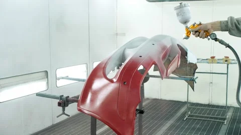Worker paints bumper of car red using air spray gun in booth Stock Footage 166576424
