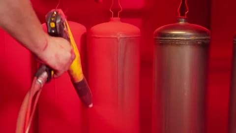 Worker paints fire extinguishers with spray gun at factory. Painting parts Video stock 250438050