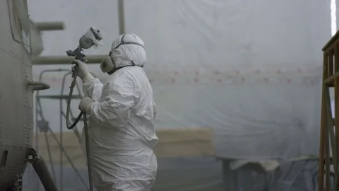 Worker Paints Helicopter Side with Sprayer in Hangar Stock Footage 72565525