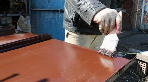 A worker paints a horizontal iron sheet brown in an outdoor workshop Stock Photos