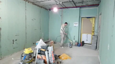 Worker paints interior walls in unfinished room during renovation process in a c Stock Footage 330156471
