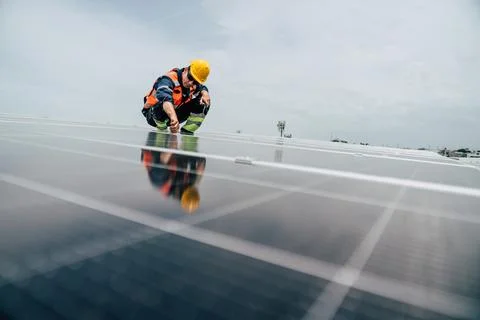Worker performs maintenance on solar panels at rooftop installation site in.. Stock Photos