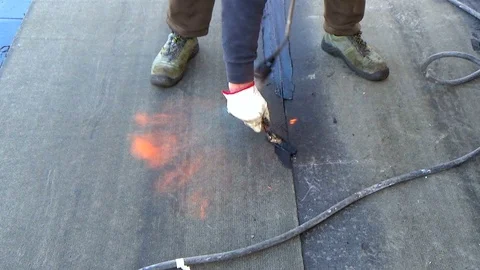 Worker performs sealing overlapping bitumen sheets on the flat roof of the bu Stock Footage 86660083