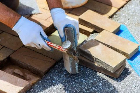Worker places bricks in driveway while using hammer during repairing surface Foto stock