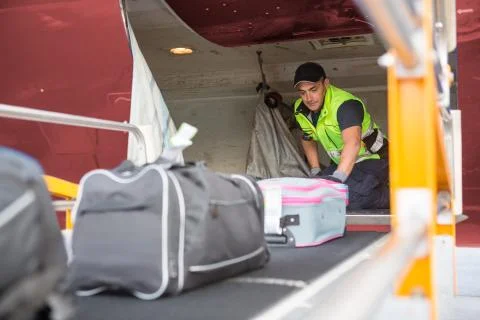 Worker Placing Baggage On Conveyor To Unload Airplane Stock Photos