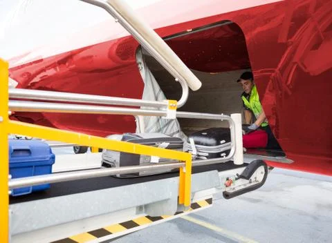 Worker Placing Baggage On Conveyor While Unloading Airplane 写真素材