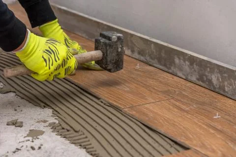 Worker placing ceramic floor tiles on adhesive surface. Stock Photos