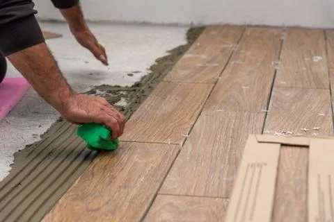 Worker placing ceramic floor tiles on adhesive surface, leveling with rubber Stock Photos