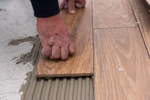 Worker placing ceramic floor tiles on adhesive surface, leveling with rubber Stock Photos