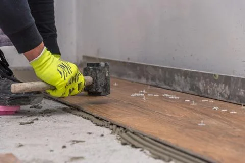 Worker placing ceramic floor tiles on adhesive surface, leveling with rubber Stock Photos