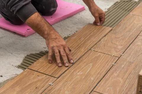 Worker placing ceramic floor tiles on adhesive surface. Stock Photos