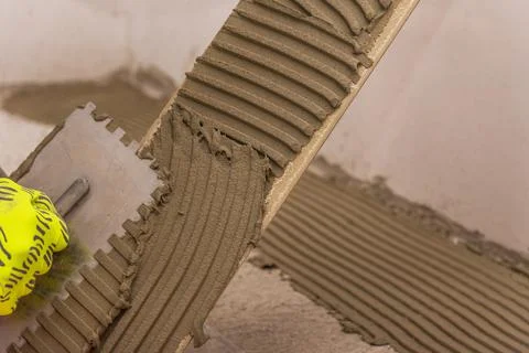 Worker placing ceramic floor tiles on adhesive surface, leveling with rubber Stock Photos