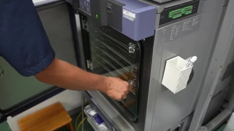 Worker placing a part tray into an environmental test oven for quality testing Stockbeeldmateriaal 340901866