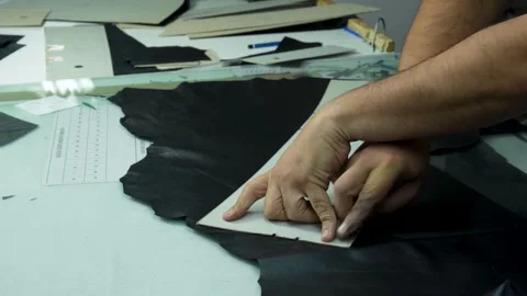 Worker Placing Pattern Template on Black Leather Hides for Cutting Stock Footage 322057589