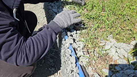 Worker placing rocks around a drainage pipe inside a gabion structure Stock Footage 308824202
