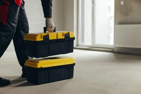 Worker Placing Tool Case Onto Stacked Case In Unfinished Room. Foto stock