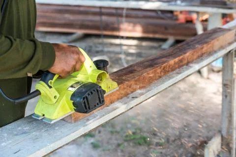 Worker planing a plank of wood with a electric plane 스톡 사진