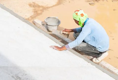 Worker plastering edge pool with trowel and water bin. Stock Photos