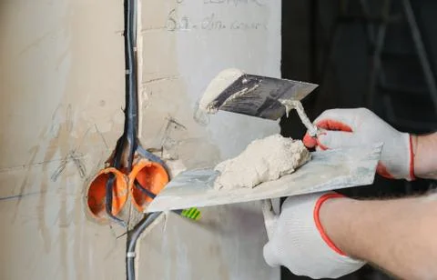 A worker is plastering the electric cables in the wall. Stock Photos