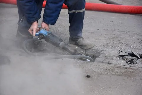 A worker with a pneumatic hammer breaks asphalt. Stock Photos