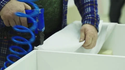 A worker with a pneumatic stapler attaches fabric to furniture Stock Footage 225140603