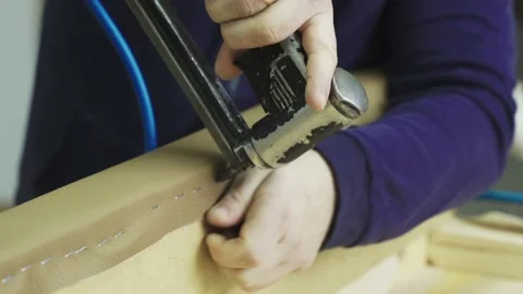 A worker with a pneumatic stapler attaches leatherette to furniture Stock Footage 223744011