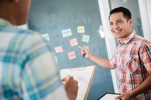 A worker pointing to paper notes on the glass wall to explain his partner Stock Photos