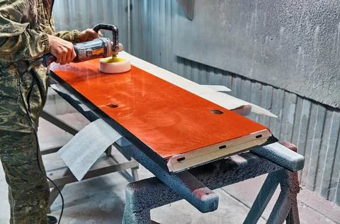 Worker polishes a red panel with a grinder. Woodworking and carpentry production Stock Photos