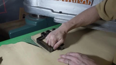 Worker positioning leather on a clicker cutting press to stamp out baseball Stock Footage 340156032
