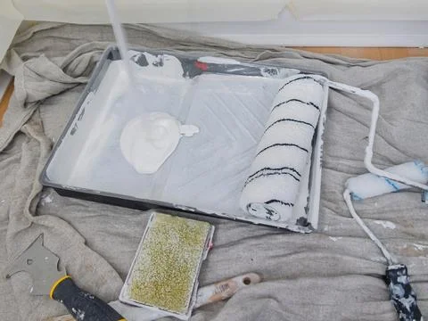 Worker pouring white paint into a paint tray covered with a plastic sheet, .. Stock Photos