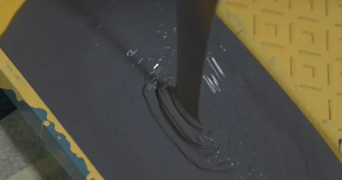 Worker pours dense dark grey paint into yellow container Stock Footage 169632059