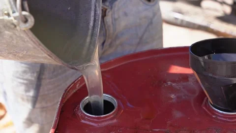 Worker pours new engine oil into an iron barrel from a bucket Stock Footage 240948911