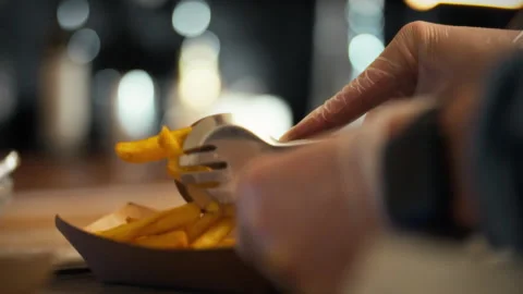 Worker prepares crispy fries using tongs for customers at a busy eatery sett Stock Footage 323869230