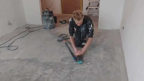 Worker prepares floor in empty room using a power tool and vacuum machine in ren Stock Footage 331245342