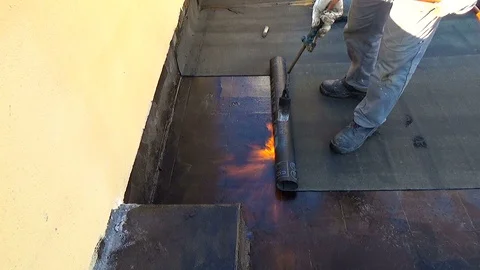Worker preparing part of bitumen roofing felt roll for melting by gas heater Stock Footage 86660204
