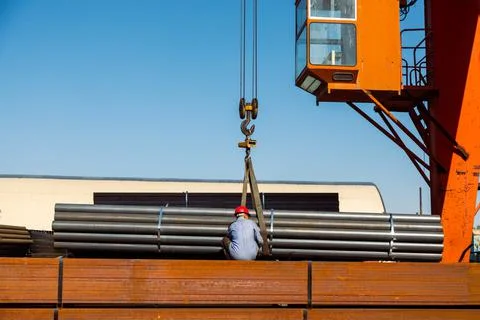 Worker preparing stack of metal pipes for transporting with gantry crane Stock Photos