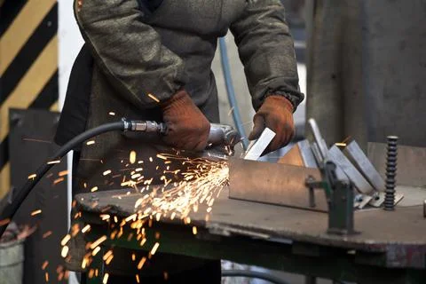 Worker processing metal, lots of sparks, against factory industrial interior Stock Photos