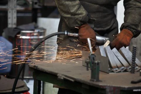 Worker processing metal, lots of sparks, against factory industrial interior Stock-Fotos