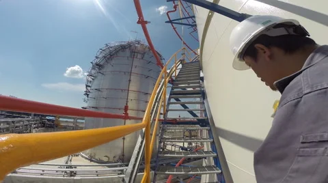 A worker production unit walks up a ladder mounted next to an oil storage tank. Stock Footage 44188349