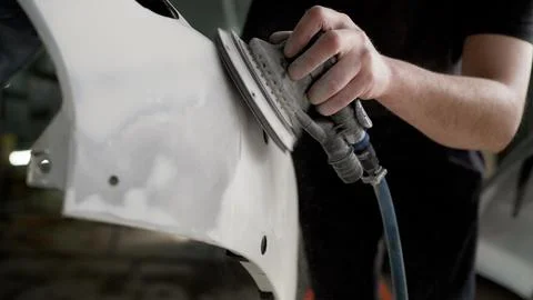 A worker professionally cleans the surface of a car bumper with a grinding Stock Photos