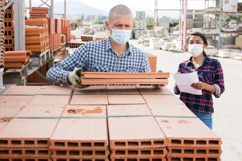 Worker in protecrive mask stacking bricks in warehouse of materials Foto stock