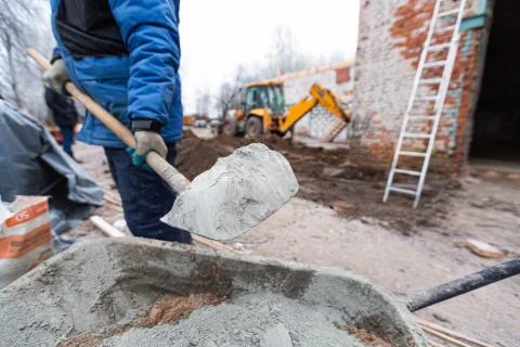 Worker in protect gloves is loading the cement by shovel to building trolley Stock Photos