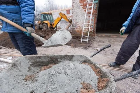 Worker in protect gloves is loading the cement by shovel to building trolley Stock Photos