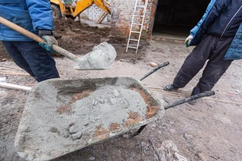 Worker in protect gloves is loading the cement by shovel to building trolley Stock Photos