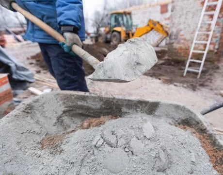Worker in protect gloves is loading the cement by shovel to building trolley Stock Photos