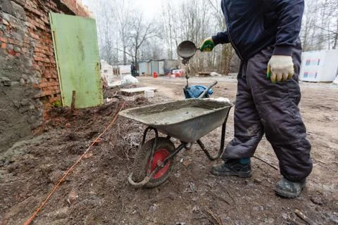 Worker in protect gloves is mixing up the liquid cement in construction trolley Stock Photos