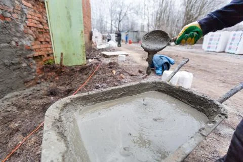 Worker in protect gloves is mixing up the liquid cement in construction trolley Stock-Fotos